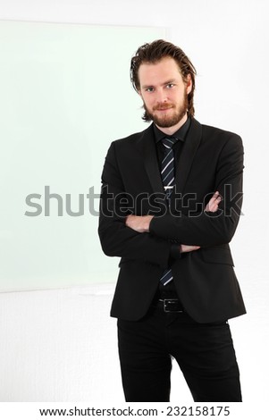 An attractive businessman wearing a suit and tie standing with a clipboard in front of a white wall with a a white board.