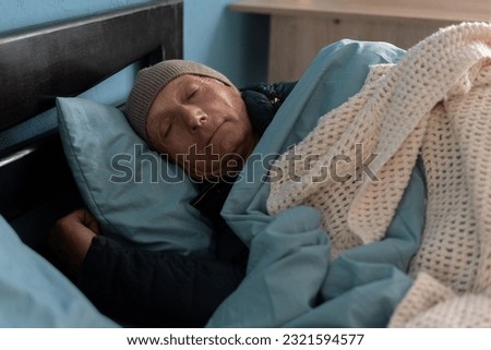 Man feeling cold at home with heating trouble, sleeping in bed wearing many clothes and cap. Copy space