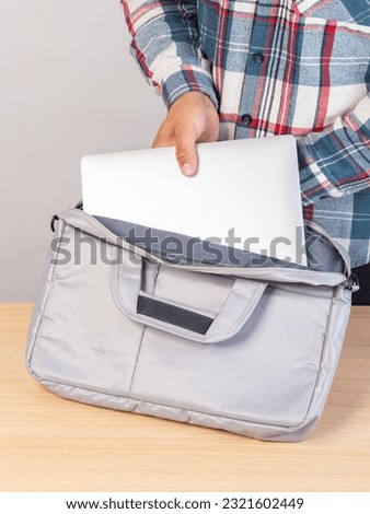 Close-up of a young male student taking out a laptop from a bag.