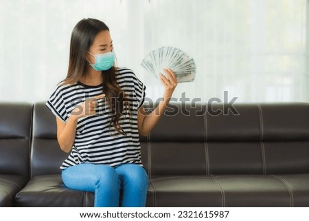 Portrait beautiful young asian woman with mask on sofa show money or cash at home Royalty-Free Stock Photo #2321615987