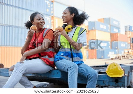 young female African factory workers or engineers having lunch and eating bread together in container warehouse storage