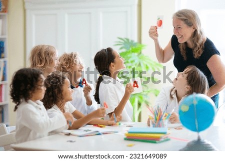 Kids go back to school. Interracial group of children of mixed age in classroom. Students learn to read and write. Preschooler or kindergarten kid with teacher. Child learning letters with flash cards Royalty-Free Stock Photo #2321649089