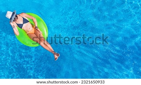 Beautiful woman in hat in swimming pool aerial drone view from above, young girl in bikini relaxes and swims on inflatable ring donut and has fun in water on tropical vacation on holiday resort