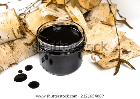 Birch tar or pitch in a jar and birch tree bark on white background. Wood tar. Liquid mineral tar from birch bark Royalty-Free Stock Photo #2321654889