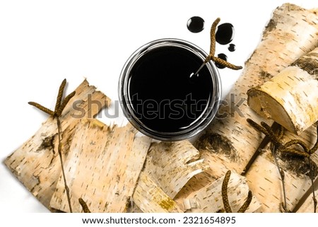 Birch tar or pitch in a jar and birch tree bark on white background. Wood tar. Liquid mineral tar from birch bark Royalty-Free Stock Photo #2321654895