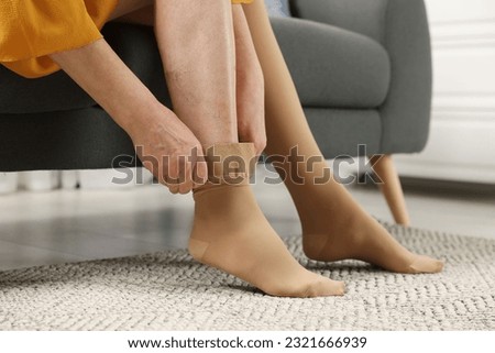Woman putting on compression stocking in living room, closeup. Prevention of varicose veins