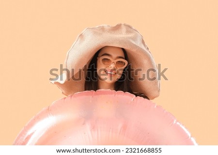 Young woman with pink inflatable ring on beige background