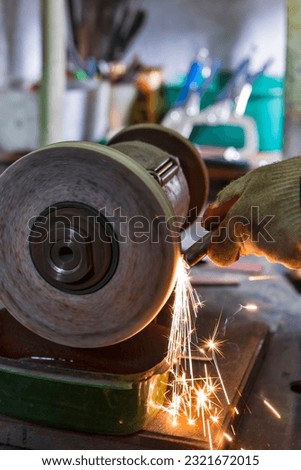 Closeup of Hands of Professional Fitter Man Using Metal Polishing Machine for Metal Rods Sharpening With Sparks in Workshop. Vertical Image Orientation