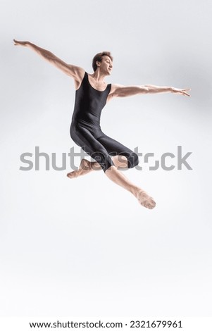 Ballet Dancer Young Caucasian Athletic Man in Black Suit Dancing in Studio Over White Background With Lifted Hands. Vertical image