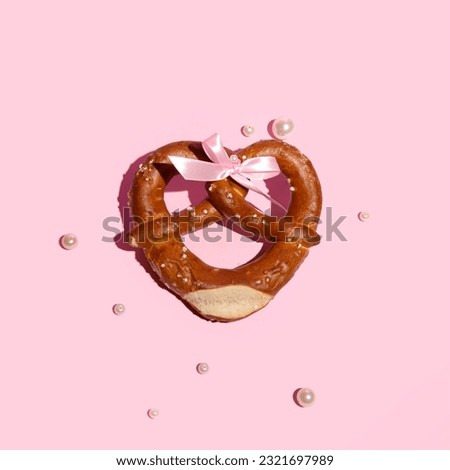 Fresh baked pretzel, heart shaped, creatively decorated with pink satin ribbon bow and pearl beads, romantic girly beer snack idea. 
