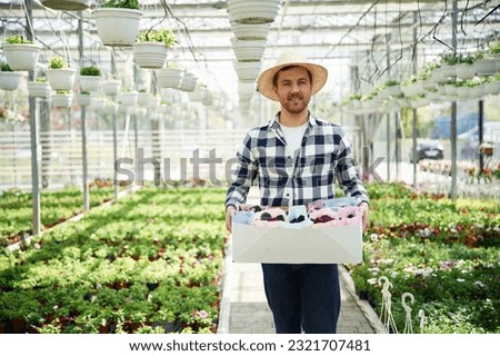 In straw hat. Florist man working in garden center. Successful employee is in a bright greenhouse.