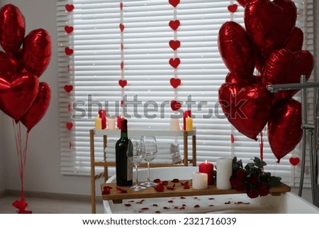 Wooden tray with wine, burning candles and rose petals on tub in bathroom. Valentine's day celebration