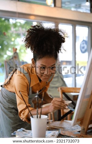 Talented African American female artist painting on canvas in art workshop. Art, creative hobby and leisure activity concept