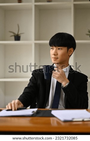 Attractive male investor in blank suit holding coffee cup and looking out of the window, daydreaming, visualizing future