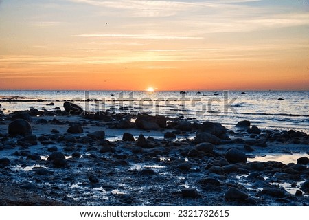 Sunset, stone beach with small and large rocks in front of the illuminated sea. Light waves. Poel island on the Baltic Sea. Nature photo from the coast