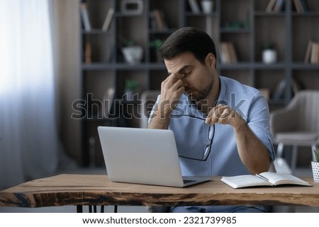 Tired eyes. Unhappy overworked millennial businessman freelancer take spectacles off massage nose bridge after long hard computer work. Exhausted young male office employee suffer of dry eye syndrome Royalty-Free Stock Photo #2321739985