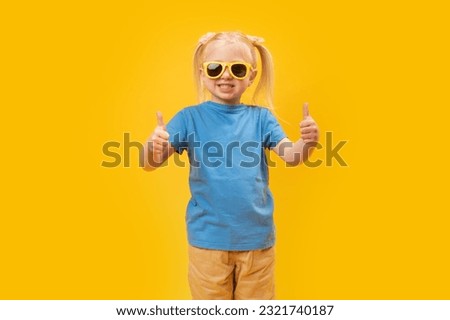 Portrait of girl in blue T-shirt and sunglasses showing thumbs up or like gesture with two hands. Copy space, mock up.