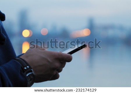 Using cellphone with defocused city lights and river reflection. Royalty-Free Stock Photo #232174129