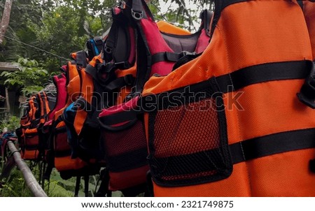 Bright orange marine life vest signal jackets close up hanging with hanger, safety on water tourism activity and watersports Royalty-Free Stock Photo #2321749875