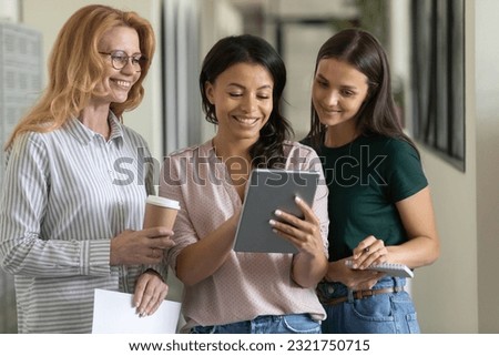 Leader showing virtual presentation on tablet to employees. Happy diverse female business group of different ages using and sharing digital device, making online video call together Royalty-Free Stock Photo #2321750715