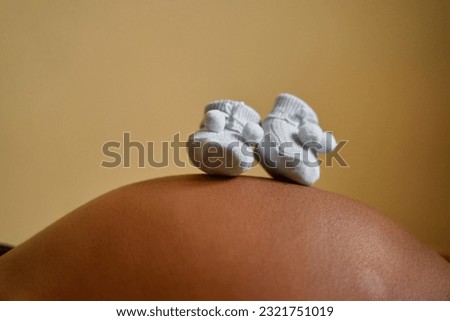pregnant woman's belly with baby boy's socks on top of it in studio Royalty-Free Stock Photo #2321751019
