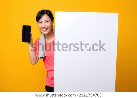 asian young sports fitness woman happy smile wearing pink sportswear standing behind the white blank banner or empty space advertisement board against yellow background. wellbeing application concept.