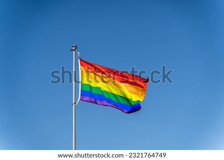The rainbow flag of the LGBTQ community flies against the backdrop of a blue clear sky