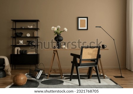 Creative composition of cozy workplace with mock up poster frame, wooden desk, rattan chair, black rack, simple lamp, vase with flowers, patterned carpet and personal accessories. Home decor. Template