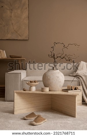 Warm and cozy composition of living room interior with travertine coffee table, modular sofa, vase with branch, wooden bench, bowl with nuts, slippers and personal accessories. Home decor. Template. Royalty-Free Stock Photo #2321768711