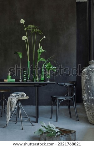Minimalist composition of japandi dining room interior with black table, glass vase with green flowers, sprinkler, plaid, chair, concrete wall and personal accessories. Home decor. Template.