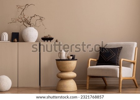 Cozy composition of living room interior with gray armchair, dark pillow, beige sideboard, wooden coffee table, vase with branch, round pillow and personal accessories. Home decor. Template. Royalty-Free Stock Photo #2321768857