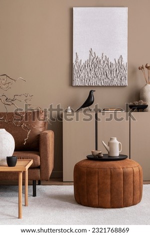 Warm and cozy living room interior with mock up poster frame, brown sofa, wooden coffee table, round pouf, beige sideboard, pitcher, cup, books and personal accessories. Home decor. Template.  Royalty-Free Stock Photo #2321768869