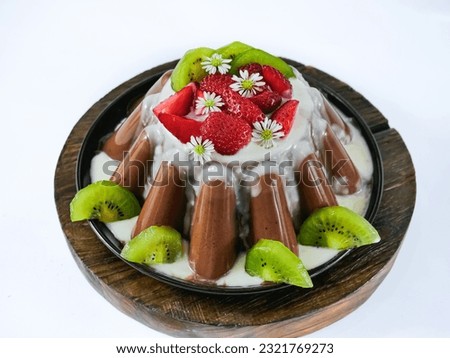 close up view of chocolate pudding made with milk, sugar, cocoa powder and jelly powder. decorated with assorted fruits. served on a plate over a wooden tray, isolated in white with copy space