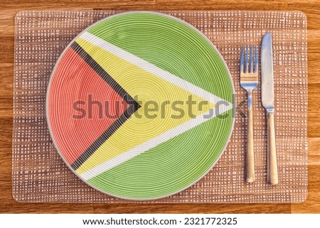 A dinner plate with the flag of Guyana on it with a fork and knife on a wooden table for international food and drink concepts