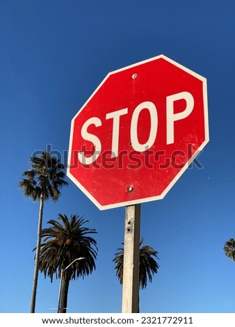 A low angle shot of a red "STOP" post sign against palm trees and a cloudless blue sky