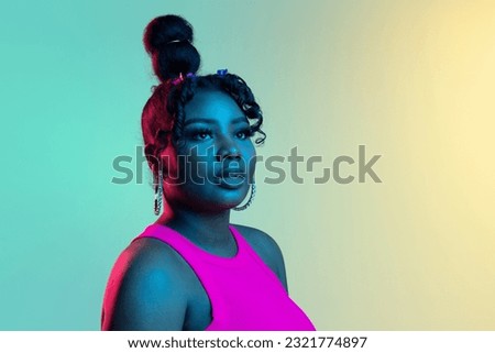 Calm, composed. Picture of young beautiful African girl, female model looking away isolated on blue green background in neon light. Concept of human emotion, facial expression. Copy space for ad.