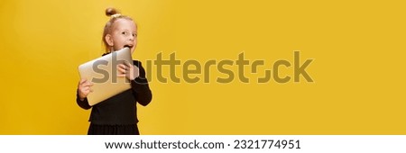 Playful, cute little girl, child posing with laptop against yellow background. Online education, remote studying and leisure. Childhood, emotions, lifestyle, fashion concept. Banner. Copy space for ad