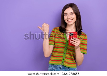 Portrait of optimistic adorable girl dressed striped cardigan hold smartphone indicating empty space isolated on violet background
