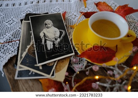 old vintage monochrome photographs scattered on rustic wooden table, Autumn composition with hot tea in mug, fallen yellow, orange leaves, concept family tree, genealogy, cozy autumn mood