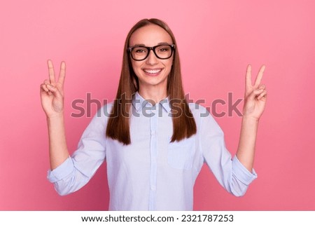 Photo of professional young girl makes peace gesture shows v sign isolated pink color background.
