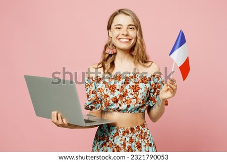 Young smiling fun caucasian tutor IT woman wear summer casual clothes hold French flag use work on laptop pc computer isolated on plain pastel light pink background studio portrait. Lifestyle concept