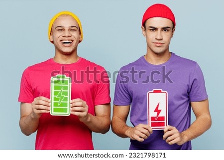Young smiling happy cheerful couple two friends men wear casual clothes together hold in hands green red charge battery card sign isolated on pastel plain light blue cyan background studio portrait Royalty-Free Stock Photo #2321798171