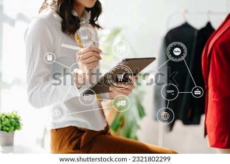 Fashion designer woman talking smart phone and using laptop with digital tablet computer in modern studio the clothes hanging on the racks morning light
