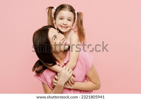 Happy fun woman wear casual clothes with child kid girl 6-7 years old. Daughter stand behind mother, hug and cuddle, looking camera isolated on plain pastel pink background. Family parent day concept