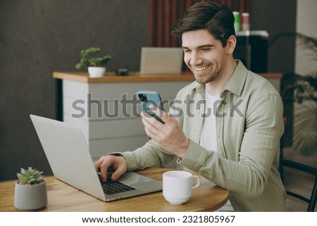 Side view happy young man wear casual clothes sits alone at table in coffee shop cafe restaurant indoors work or study on laptop pc computer use cell phone. Freelance mobile office business concept Royalty-Free Stock Photo #2321805967