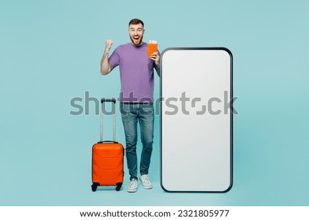Traveler winner man wear casual clothes hold suitcase passport ticket big huge blank screen mobile cell phone isolated on plain green background. Tourist travel abroad in free spare time rest getaway