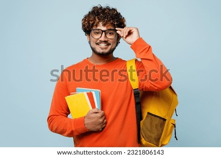 Young smiling happy teen Indian boy student wear casual clothes glasses backpack bag hold books look camera isolated on plain pastel light blue cyan background. High school university college concept