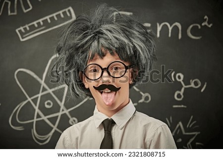 A funny cute child in glasses, with a mustache and in a wig, poses like a little professor of physics. Black chalkboard background. Education and early development. Out of the box thinking.