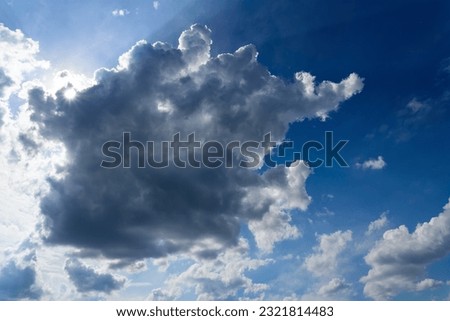 Cloudy sky with upcoming rain showers above Sauerland, Germany. Panoramic view with dramatic sunlight, contrasting dark and white clouds and blue to bright background with summer weather conditions.  Royalty-Free Stock Photo #2321814483