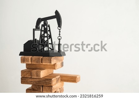 Crude oil pump jack on wood block game white wall background copy space. World petroleum, energy industry and trading in economic recession crisis, crude oil level of price cap and revenue reduce.